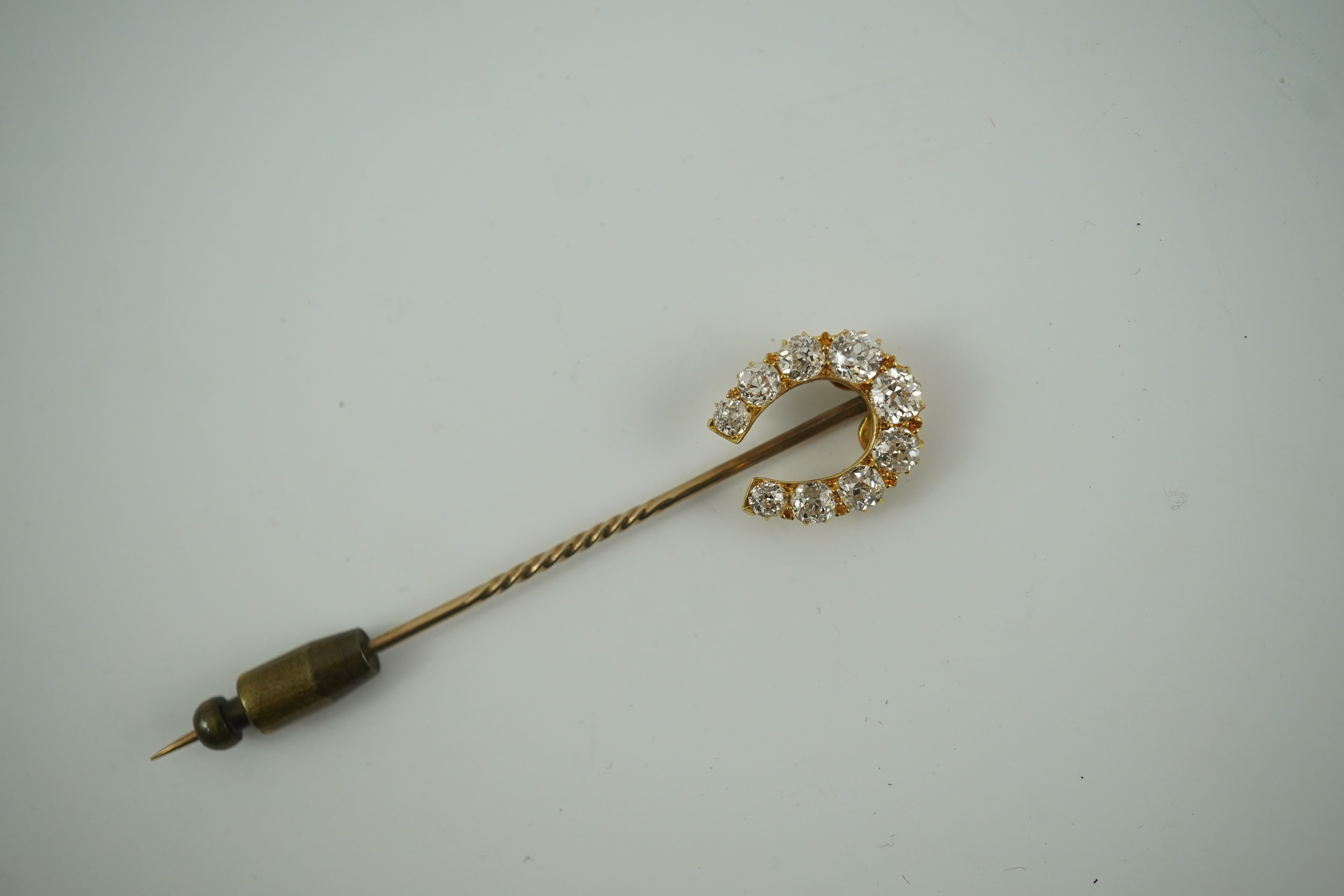 An early 20th century gold and nine stone graduated old cut diamond set horseshoe stick pin